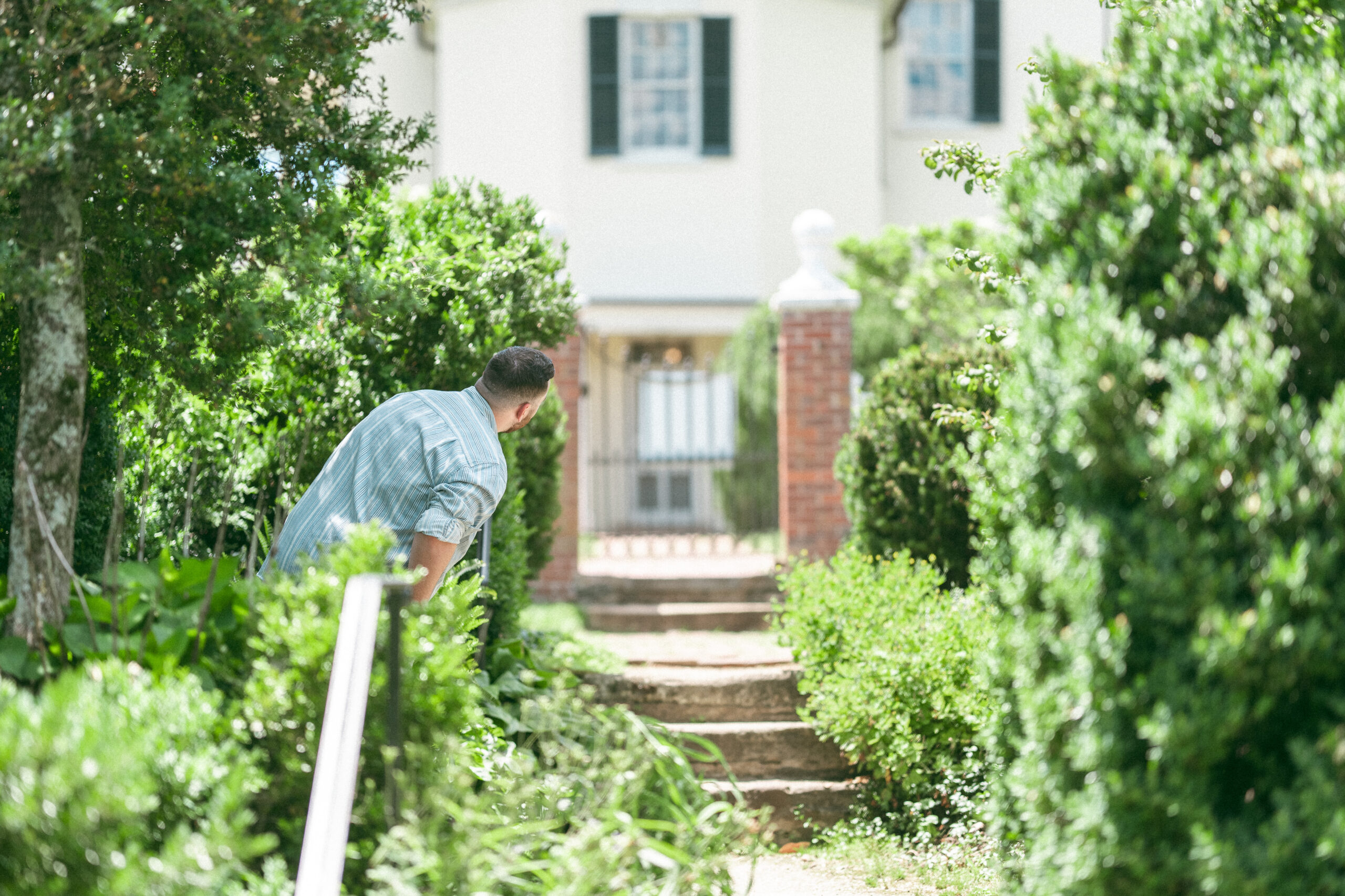 Groom-to-be peeking around the garden path before the proposal.