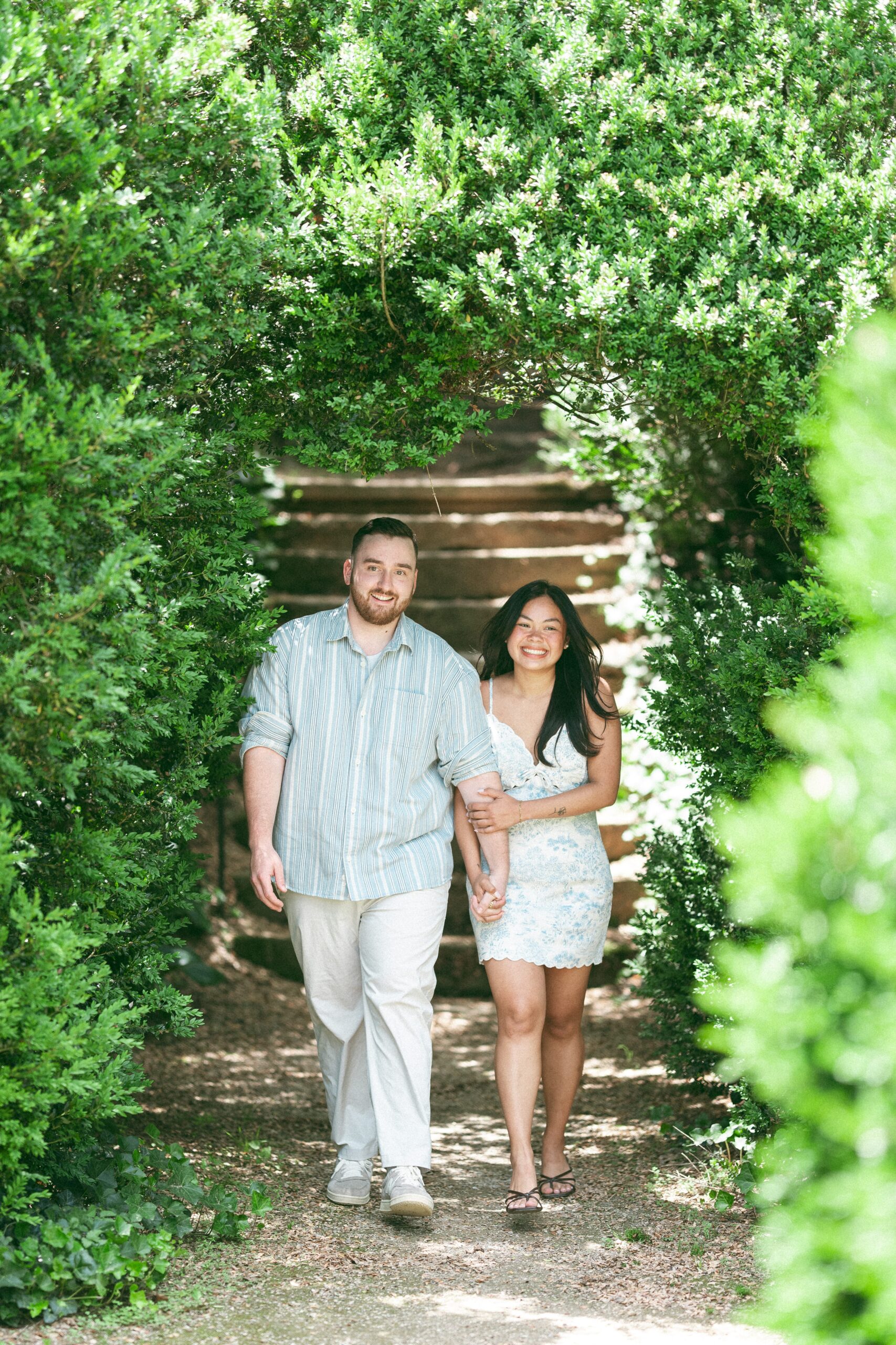 Couple walking hand in hand through a lush garden pathway during their Northern Virginia proposal.