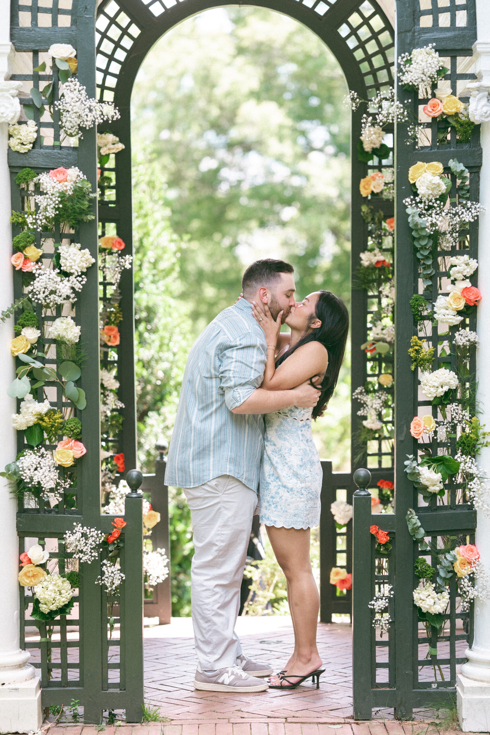 Couple sharing a kiss beneath a floral garden arbor after their proposal.