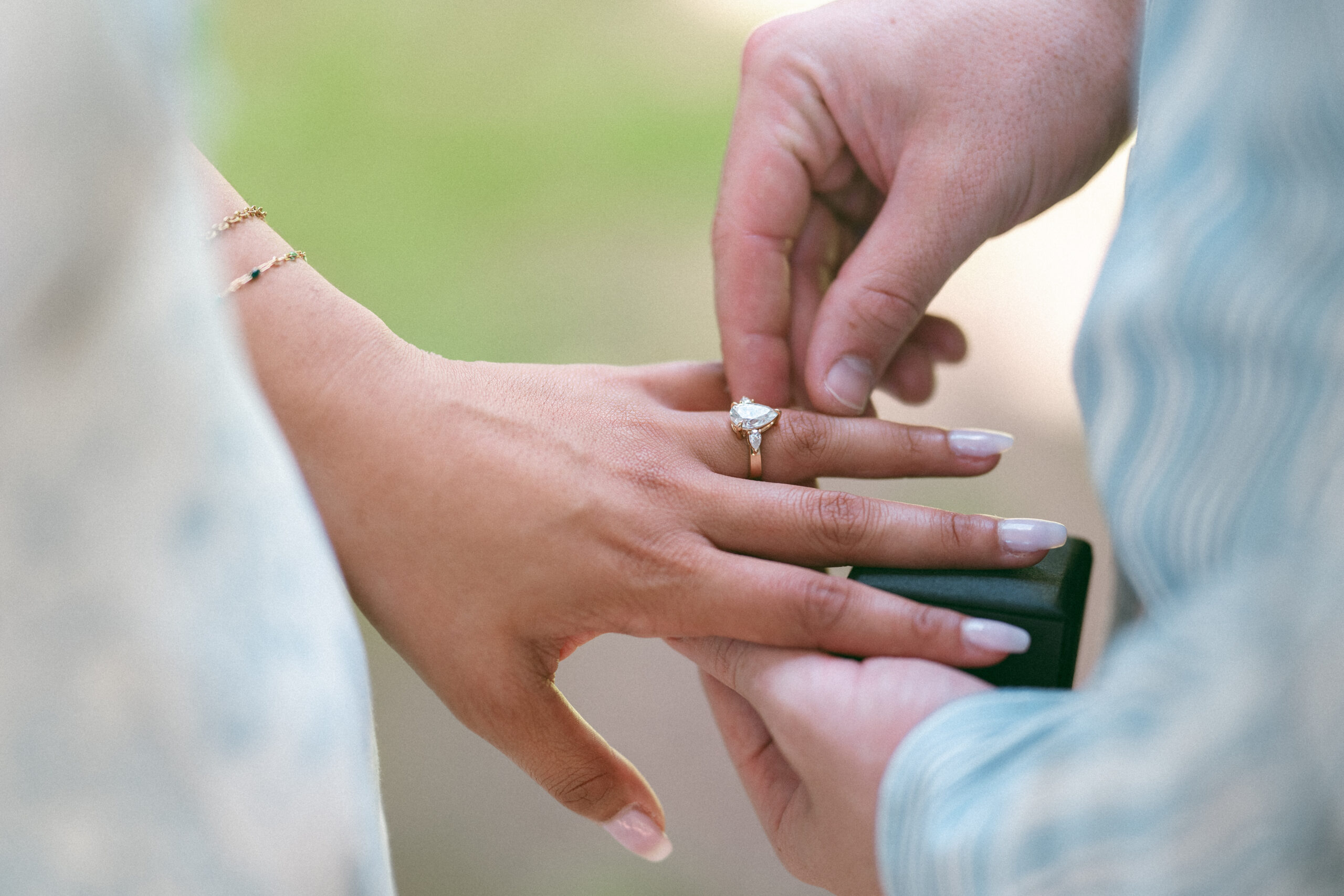 Close-up of an engagement ring being placed on the bride-to-be's finger.