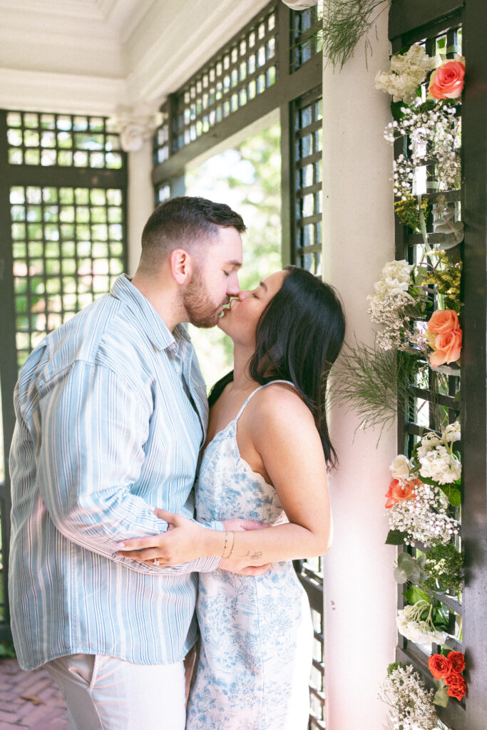 Newly engaged couple sharing a kiss beneath the garden arbor.