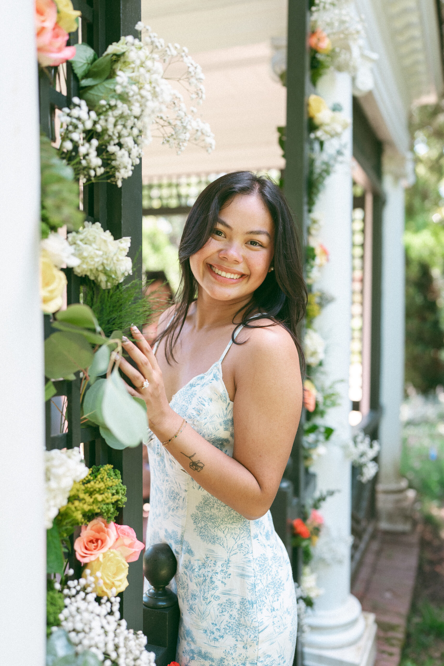 Bride-to-be smiling beside the floral arbor after getting engaged.