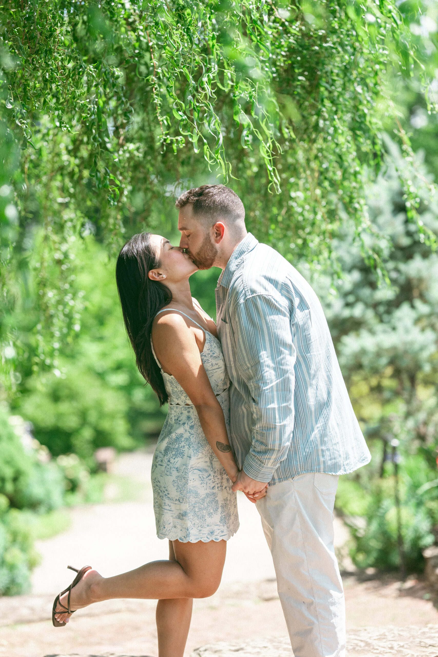 Couple kissing beneath cascading greenery while celebrating their engagement.
