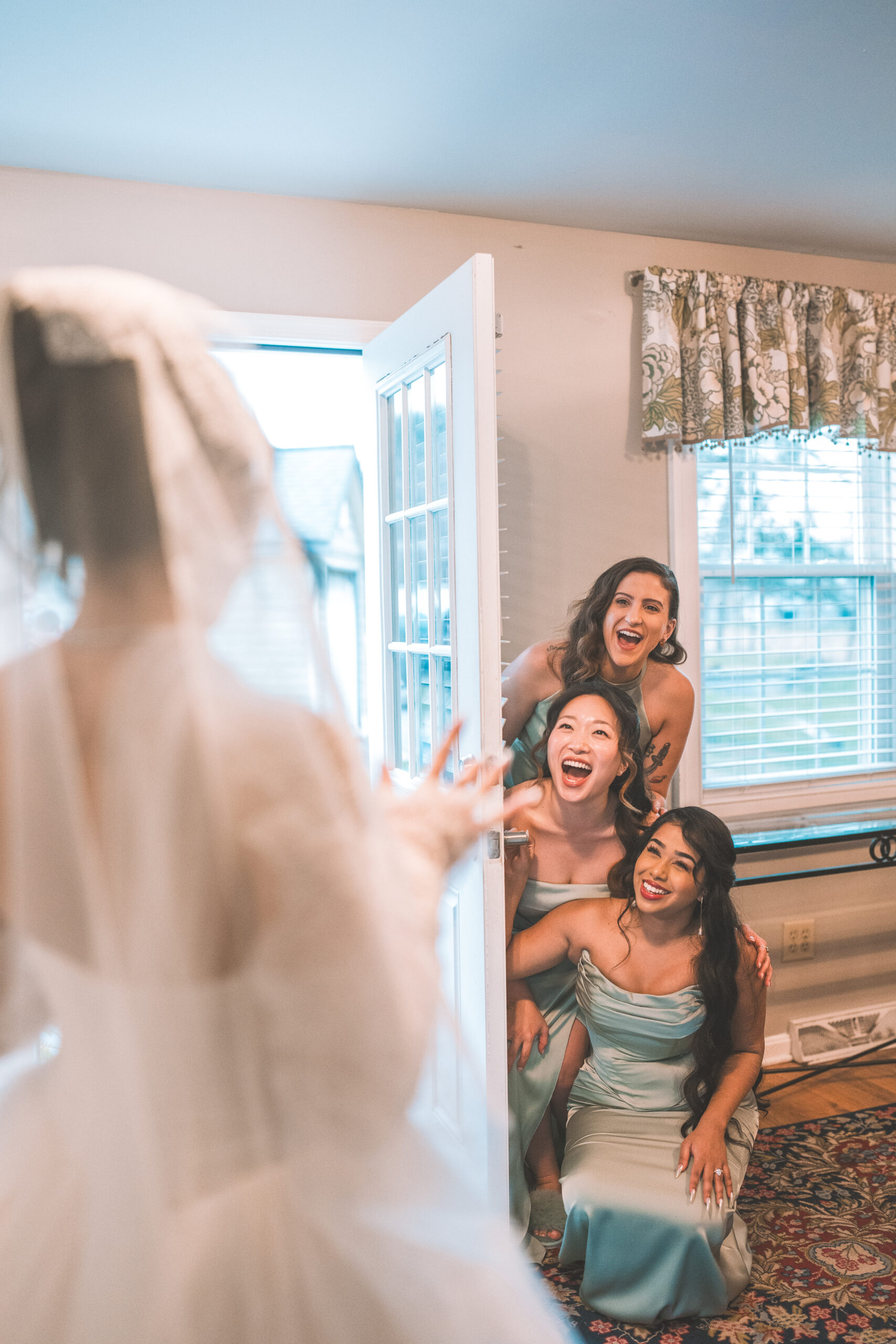 Bridesmaids laughing together as they see the bride dressed and ready for the wedding.