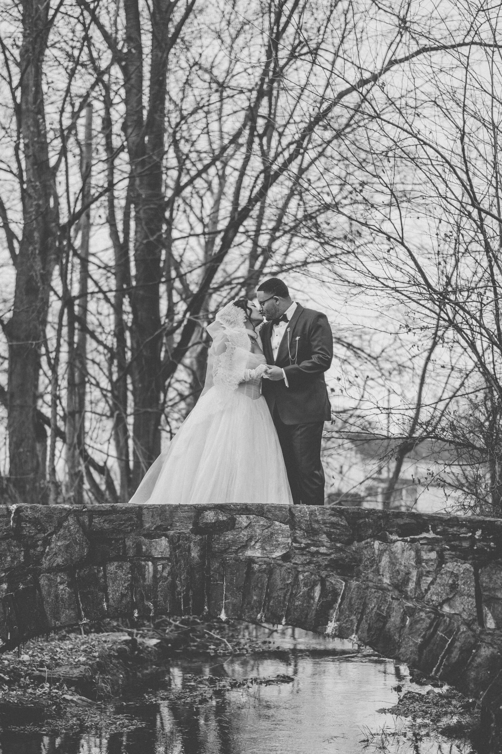 Black-and-white wedding portrait of the bride and groom kissing on a stone bridge at Cameron Estate Inn.