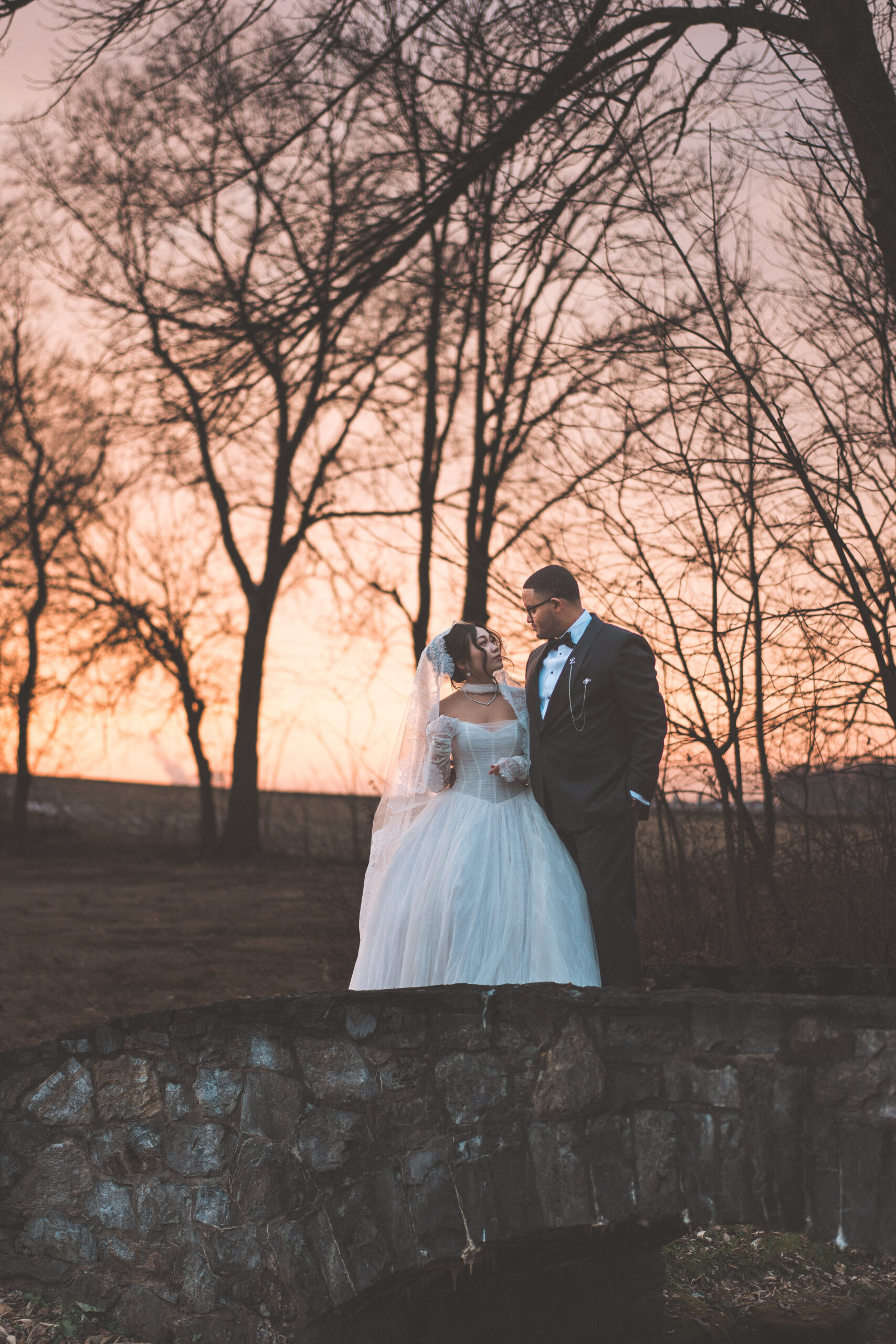 Bride and groom standing together at sunset among bare trees during their Cameron Estate Inn wedding portraits.