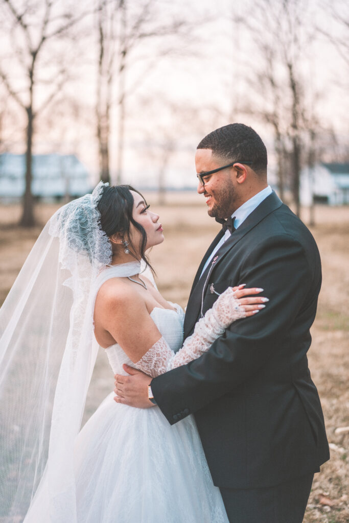Close-up outdoor portrait of the bride and groom smiling at each other in their wedding attire.