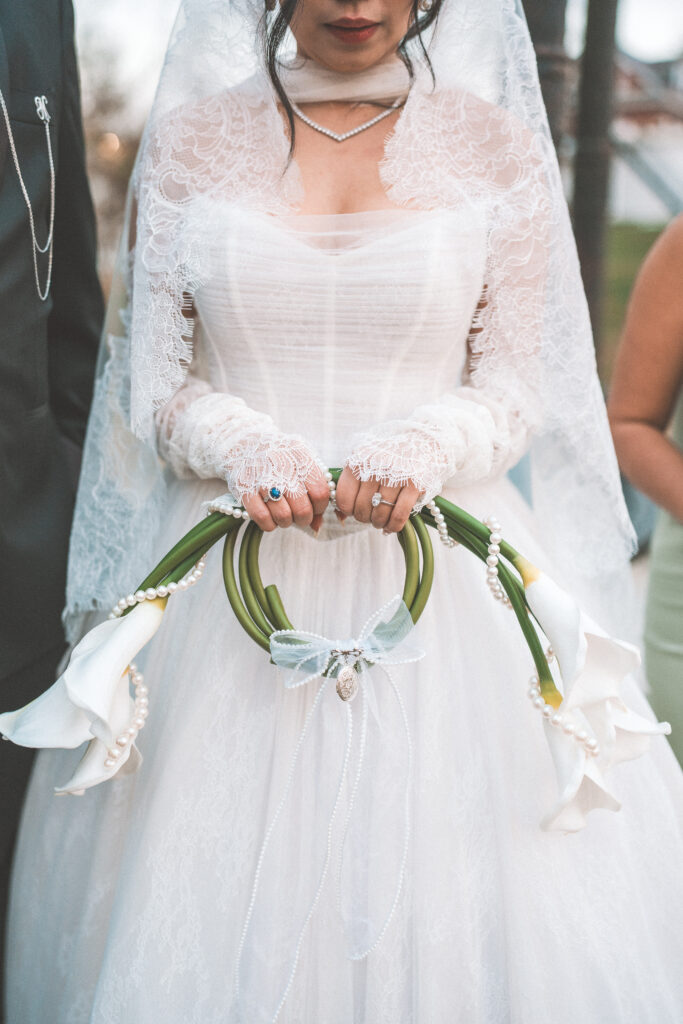 Close-up of the bride holding a white calla lily bouquet decorated with pearls and delicate ribbon details.