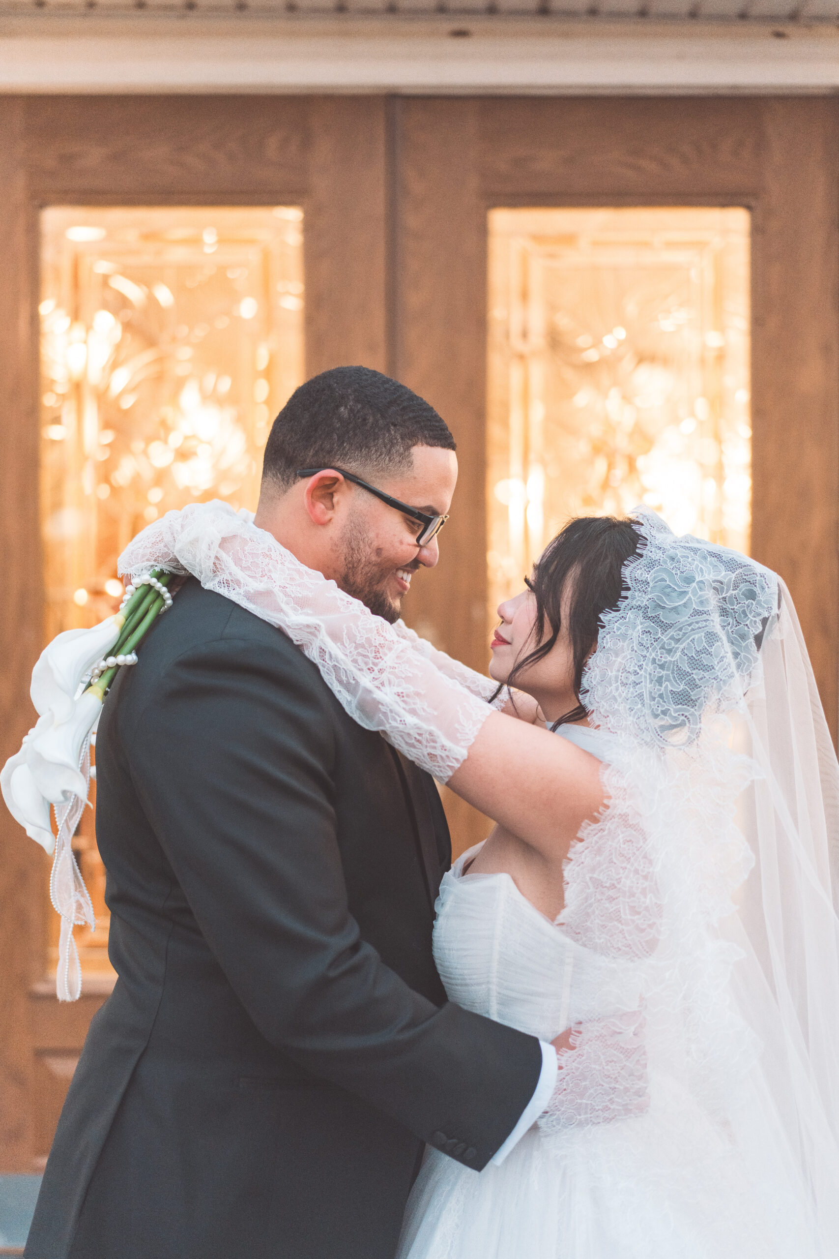 Bride and groom embracing in front of warmly lit doors during their Cameron Estate Inn wedding.
