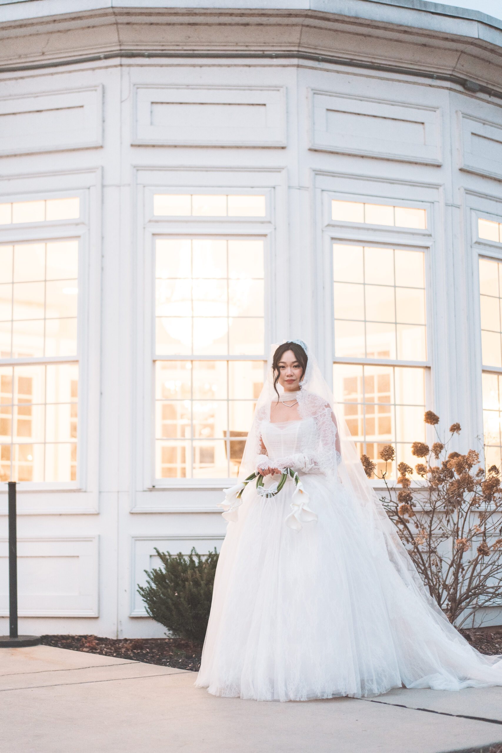 Bride posing outside Cameron Estate Inn in her lace veil and wedding gown with softly lit windows behind her.