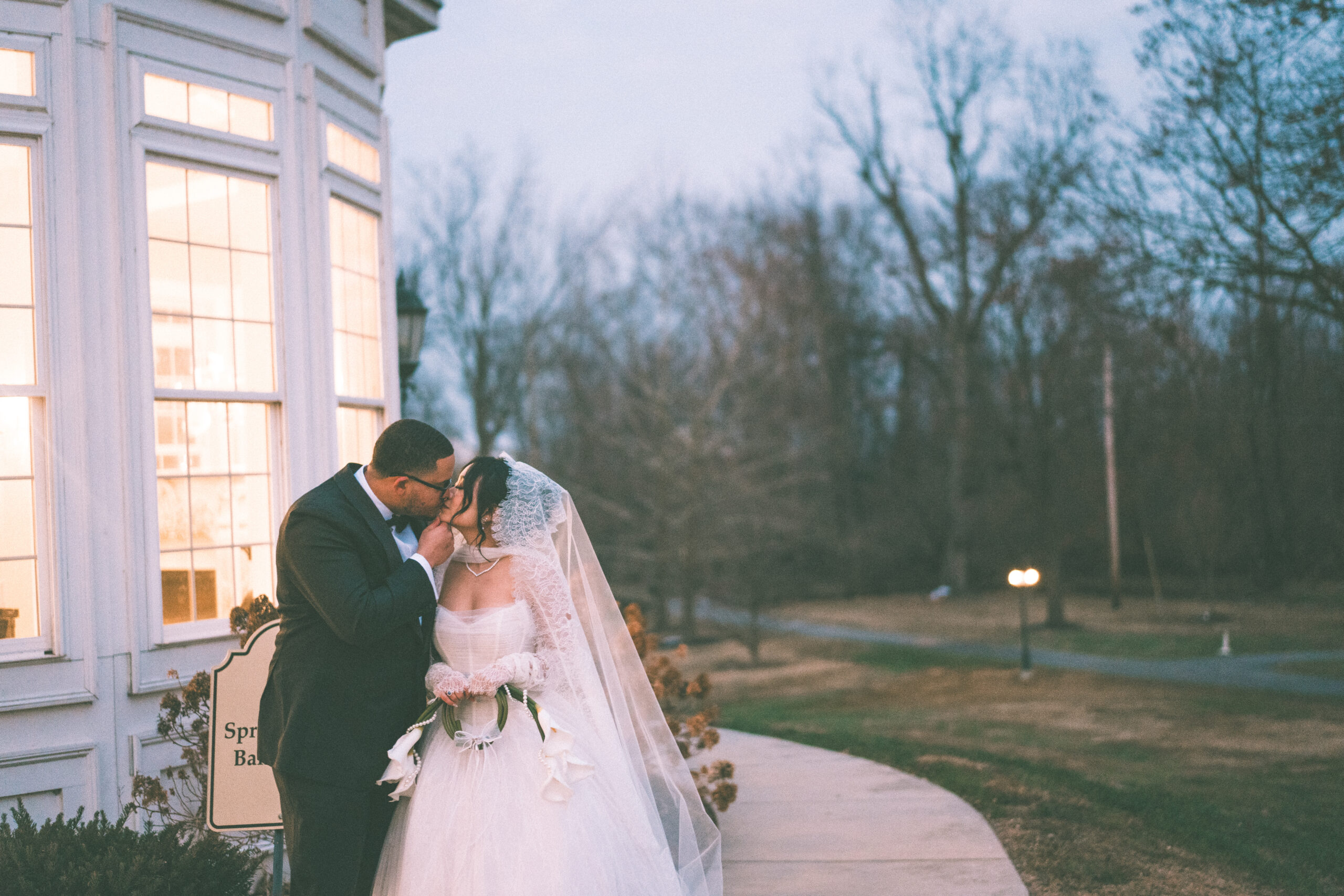 Bride and groom sharing a kiss outside Cameron Estate Inn with warm light glowing through the venue windows.