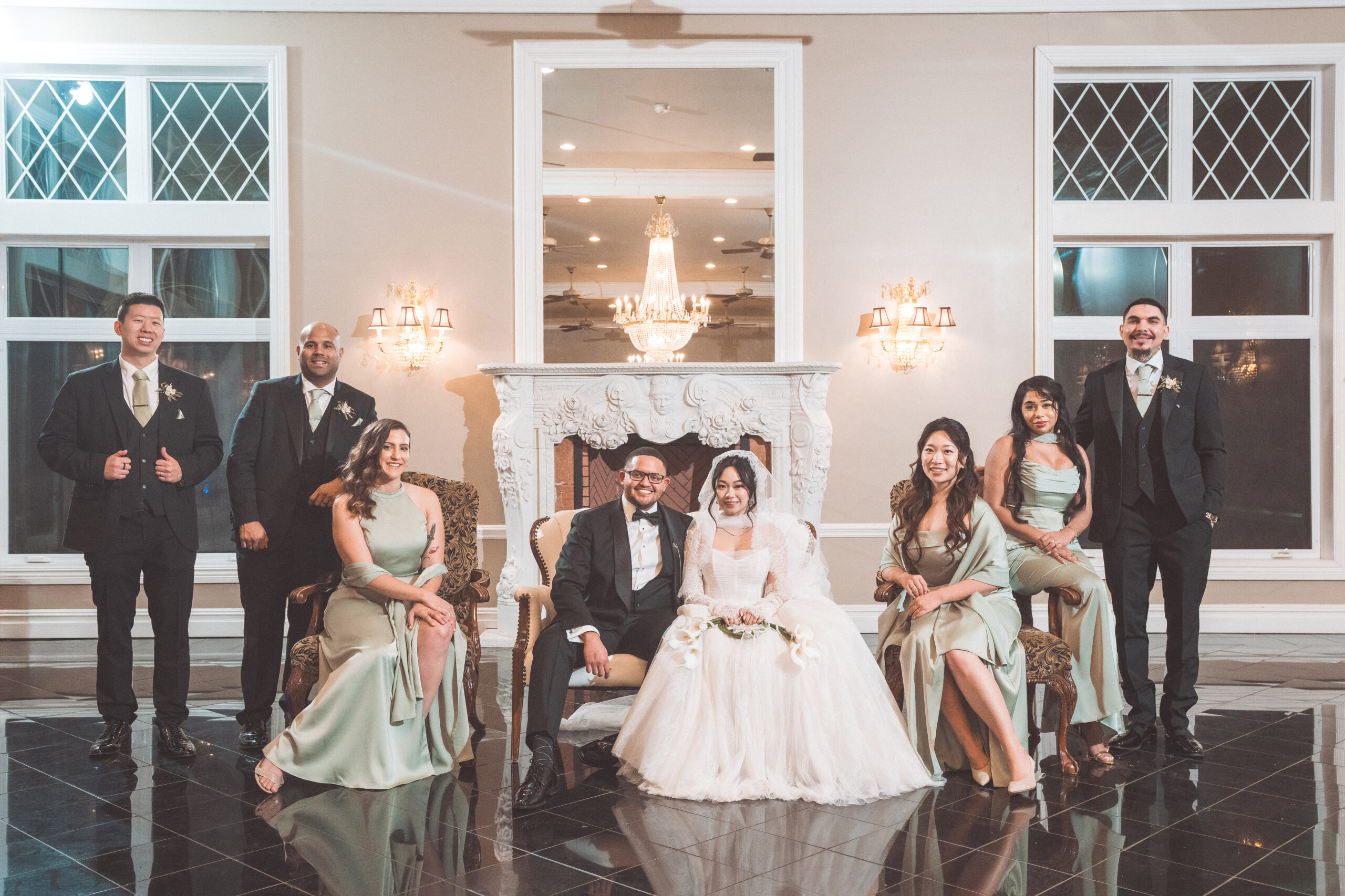 Wedding party posed with the bride and groom in front of an ornate fireplace and chandeliers at Cameron Estate Inn.