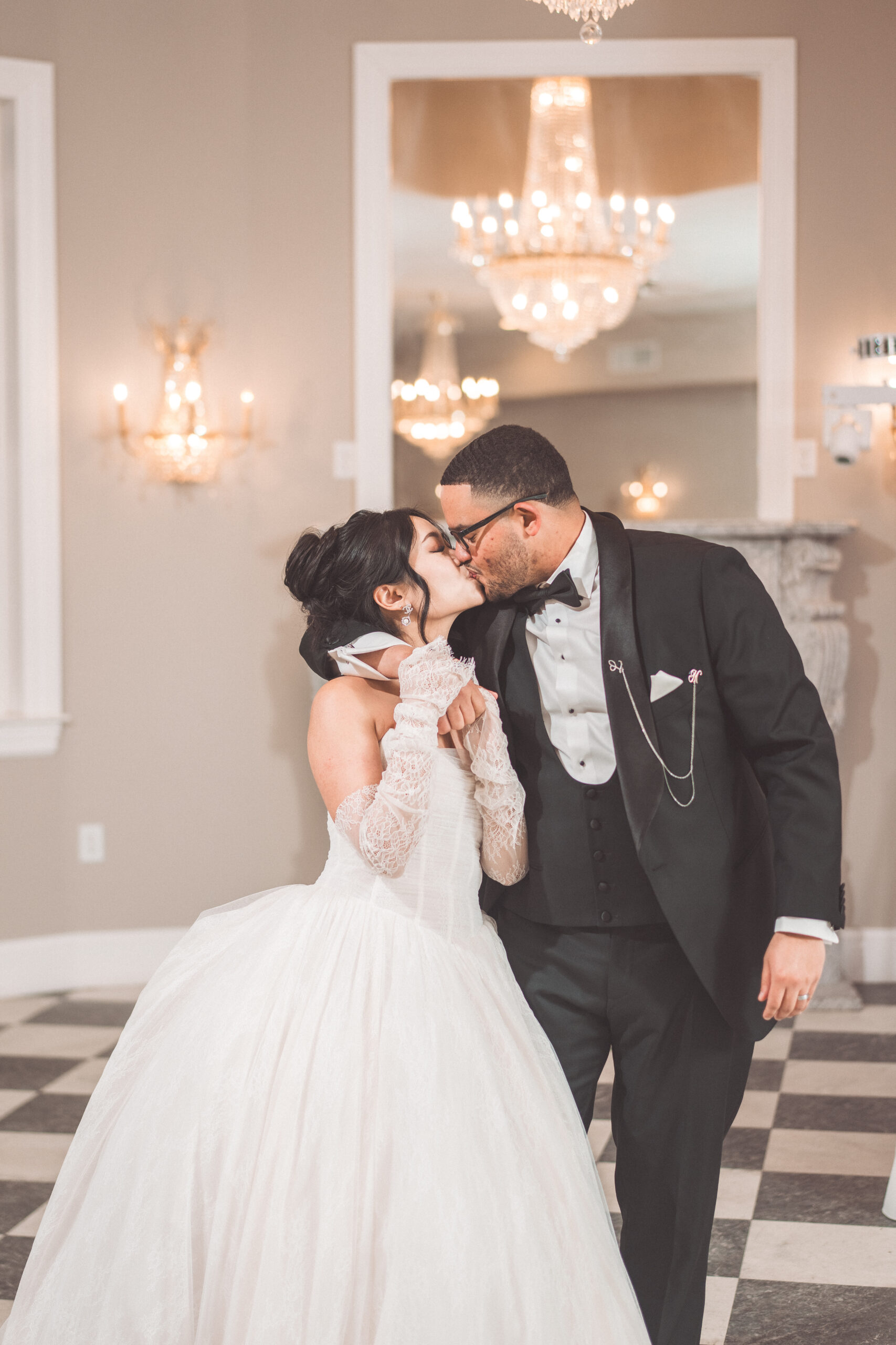 Bride and groom sharing a kiss indoors beneath elegant chandeliers during their wedding day.