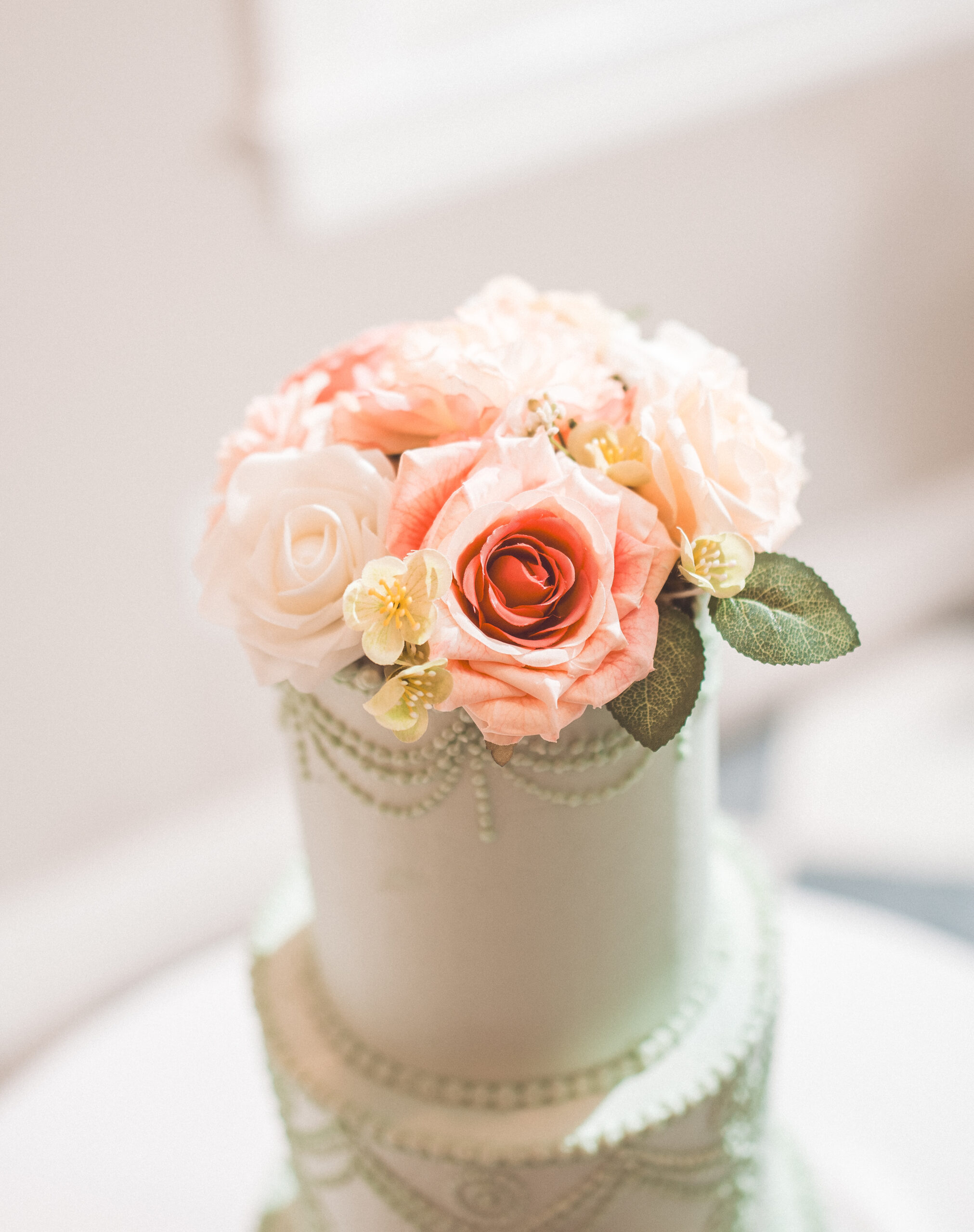A close up of a wedding cake with pink and white roses on the top teir.