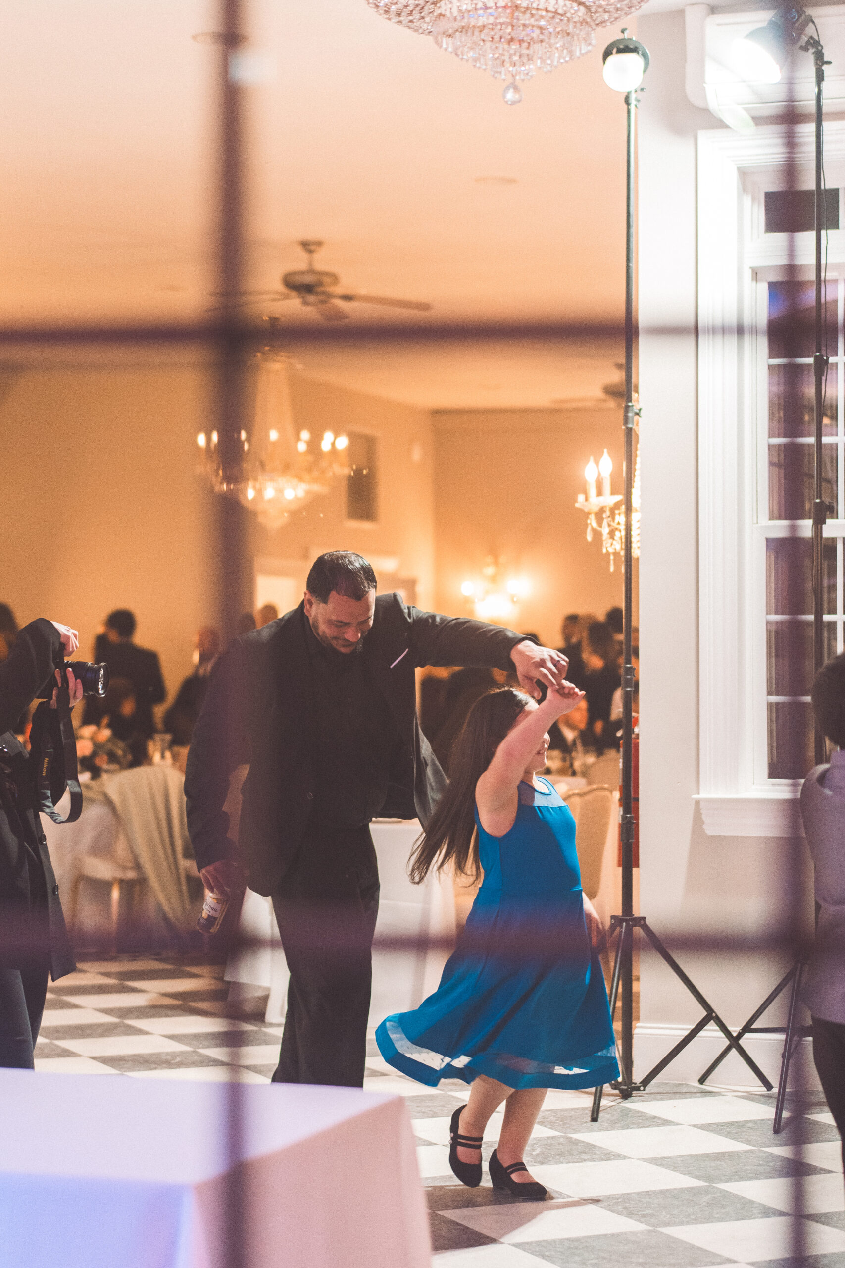 A man twirls a little girl in a blue dress during the wedding reception.