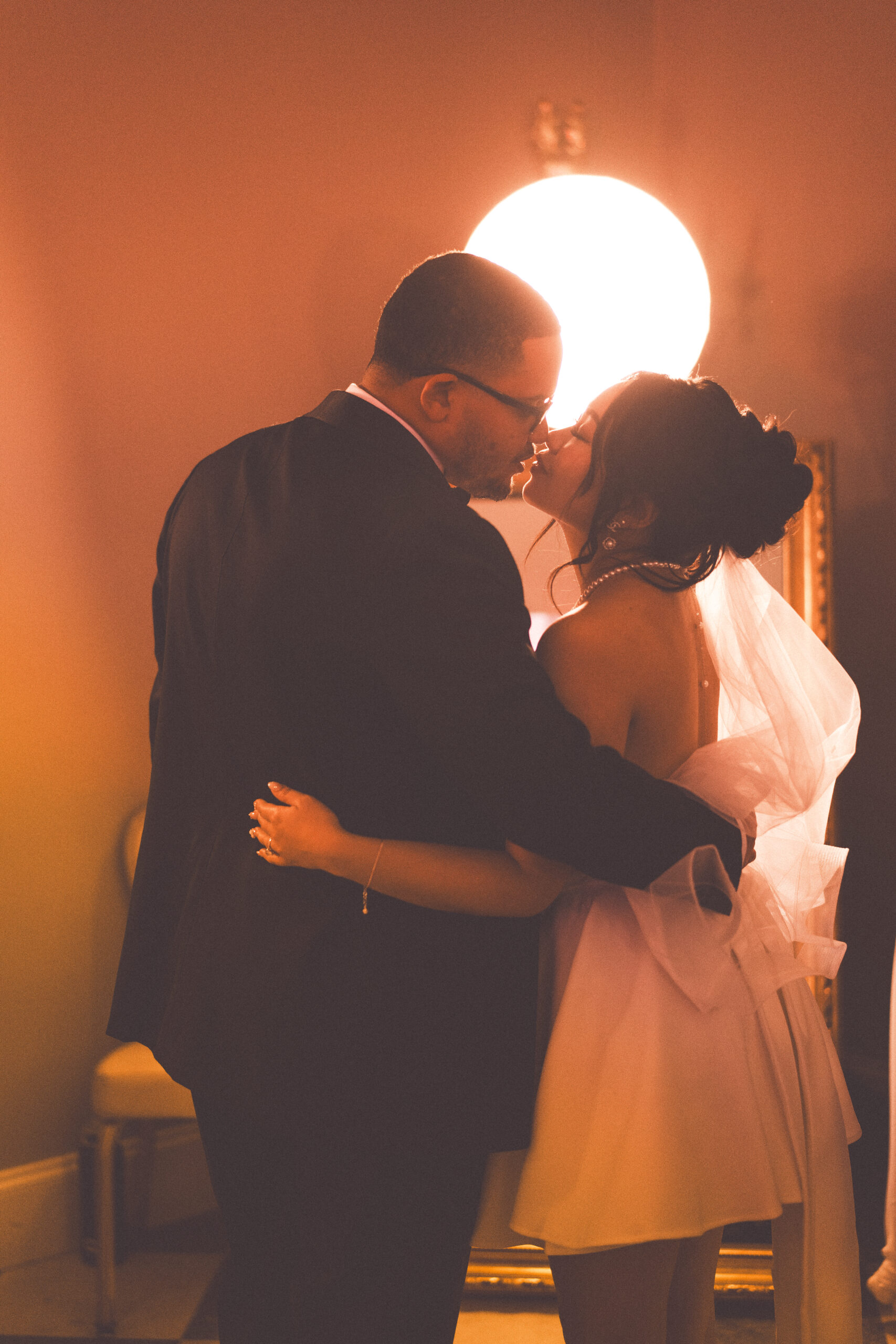 Bride and groom sharing a quiet kiss in warm indoor light during their wedding reception.