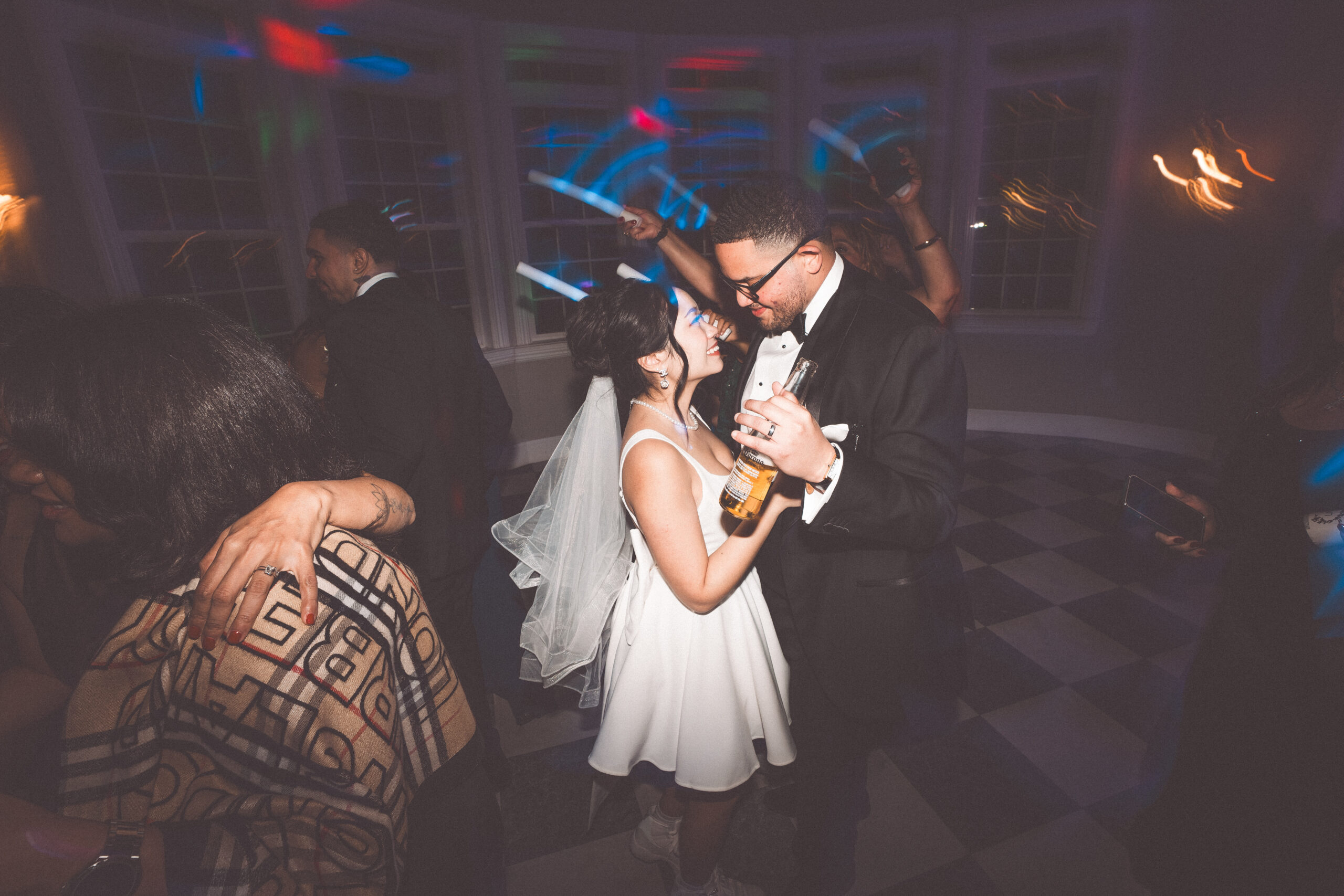 Bride and groom dancing together among guests under colorful lights during their wedding reception.