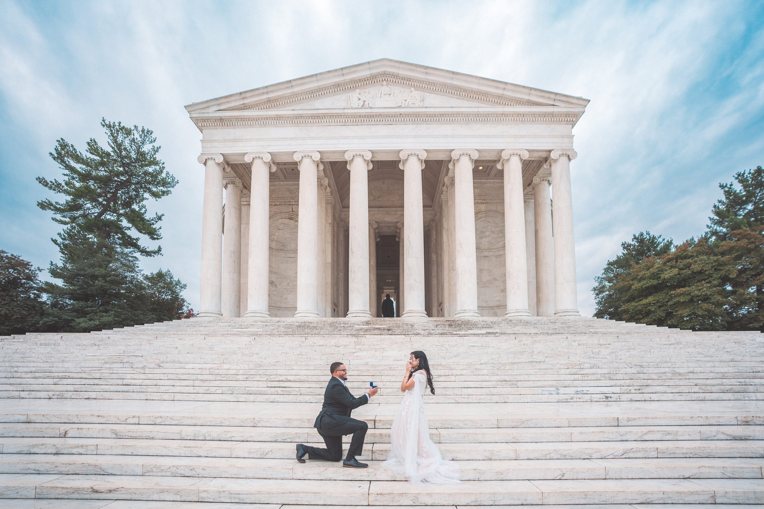 Surprise proposal on the steps of the Jefferson Memorial with the man kneeling and holding out an engagement ring.