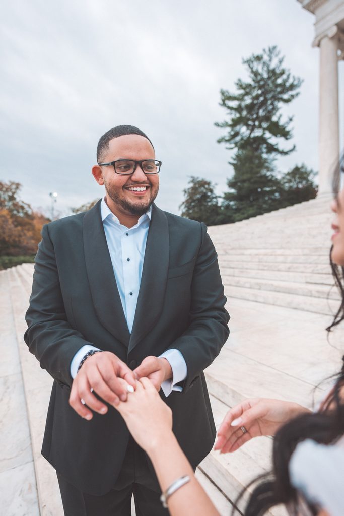 Newly engaged man smiling and holding his fiancée’s hands after proposing during their Jefferson Memorial engagement photos.