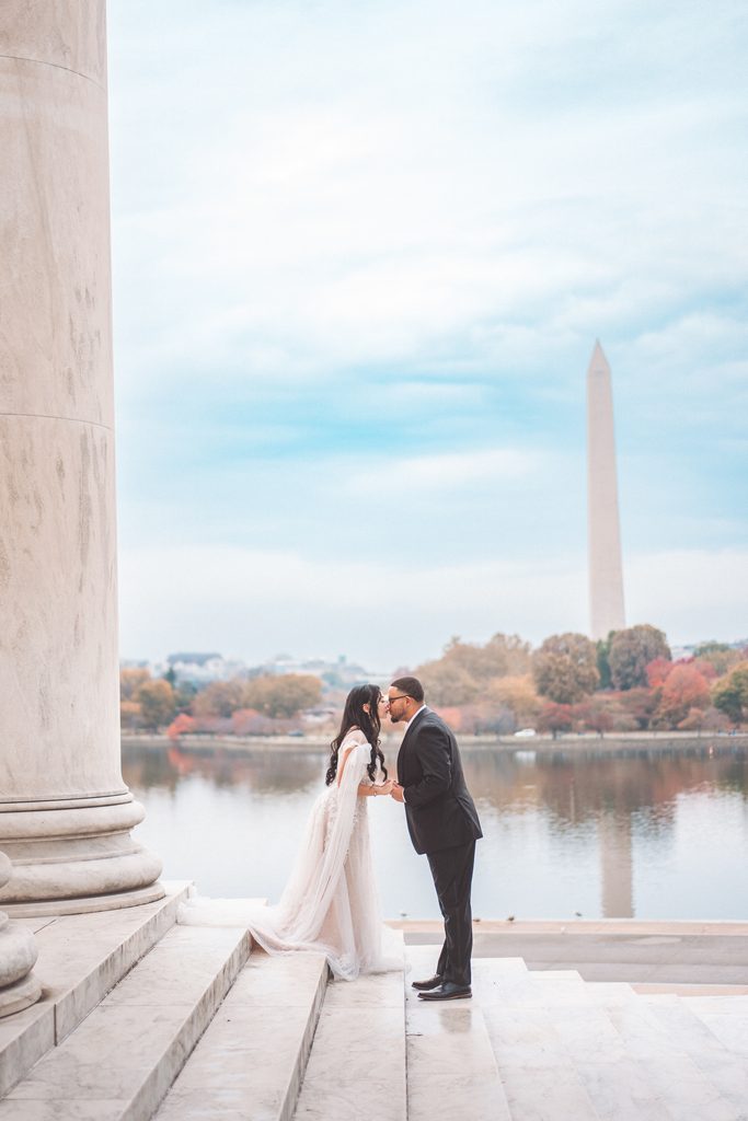 Couple kissing on the Jefferson Memorial steps with the Washington Monument across the Tidal Basin during their Jefferson Memorial engagement photos.