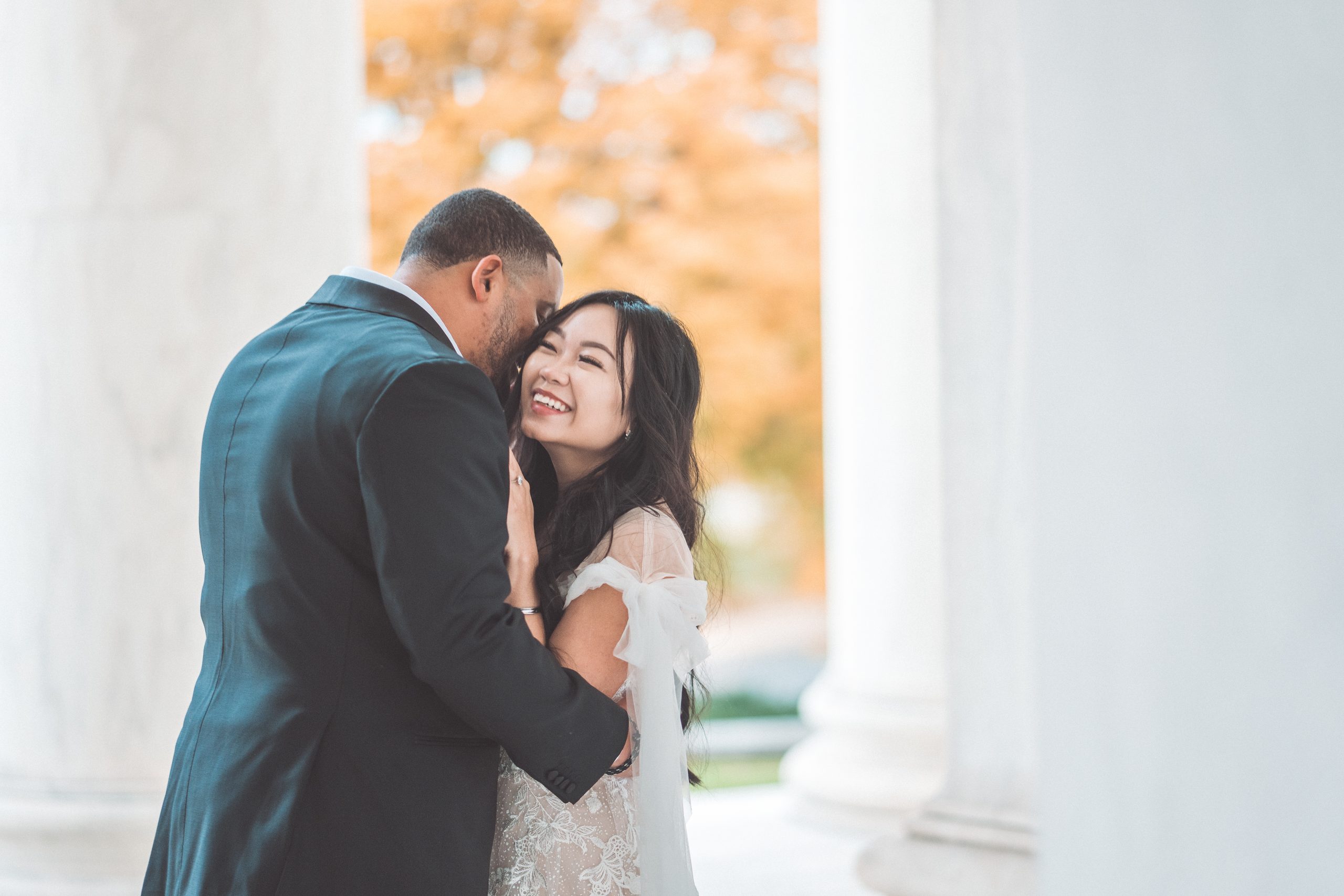 Engaged couple laughing and embracing between the marble columns during their Jefferson Memorial engagement photos.