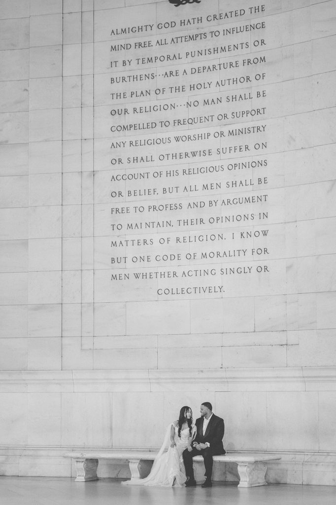 Black-and-white Jefferson Memorial engagement photos of a couple sitting together beneath the memorial’s engraved stone wall.
