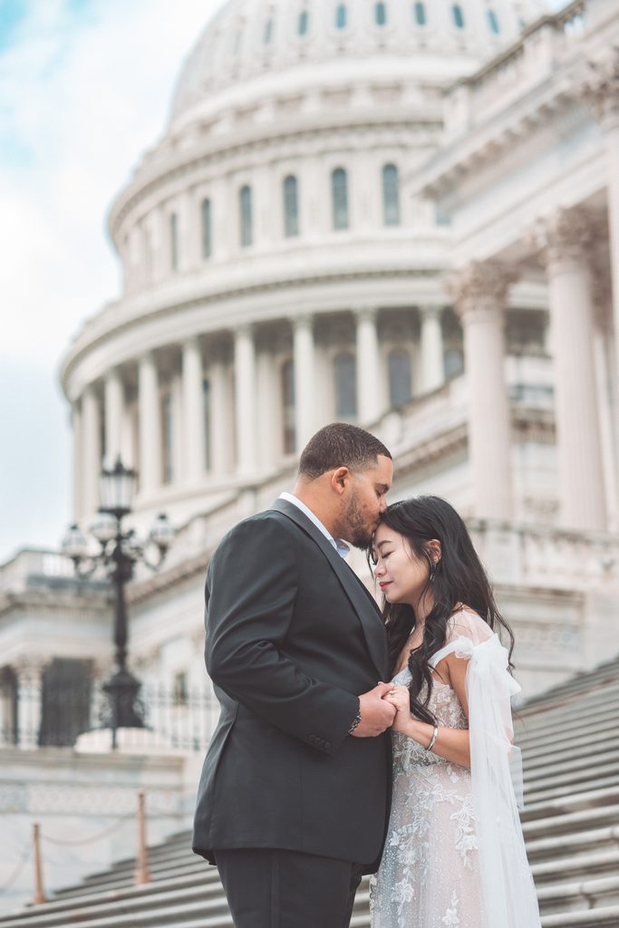 Groom-to-be kissing his fiancée on the forehead while holding hands in front of the U.S. Capitol.