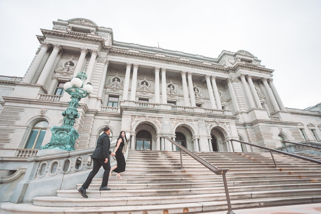 Wide engagement portrait of a couple walking up the grand steps of the Library of Congress in Washington DC.