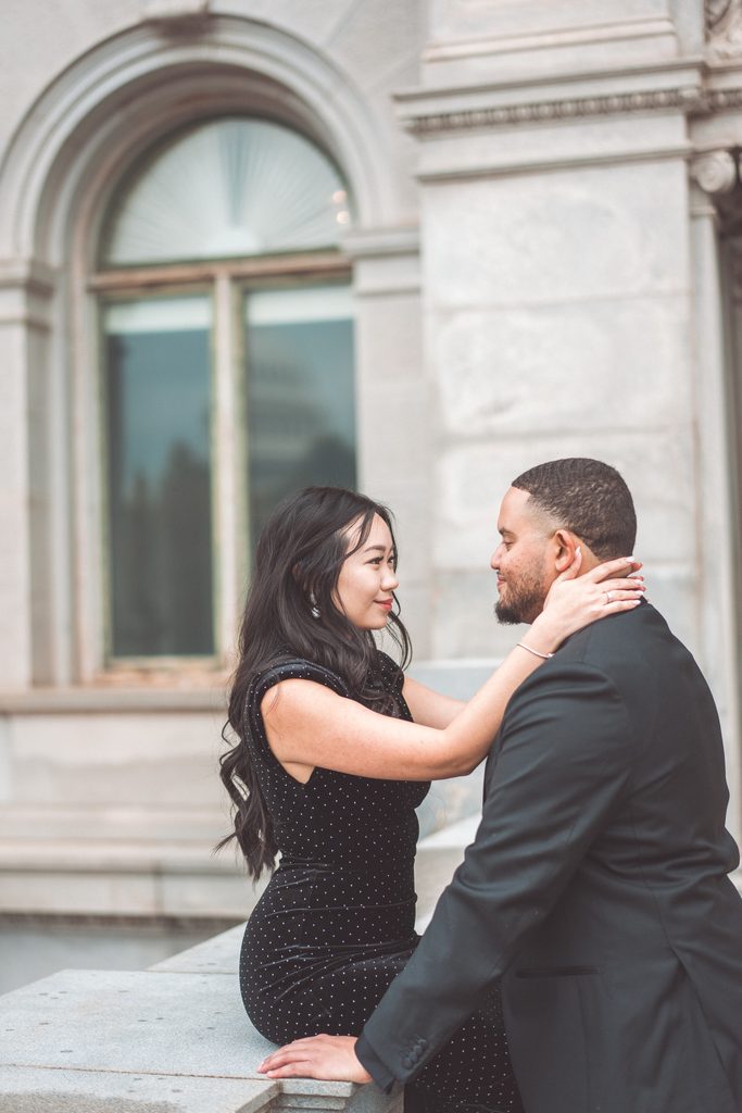 Couple sitting together as the bride-to-be holds her fiancé’s face during their Jefferson Memorial engagement photos.