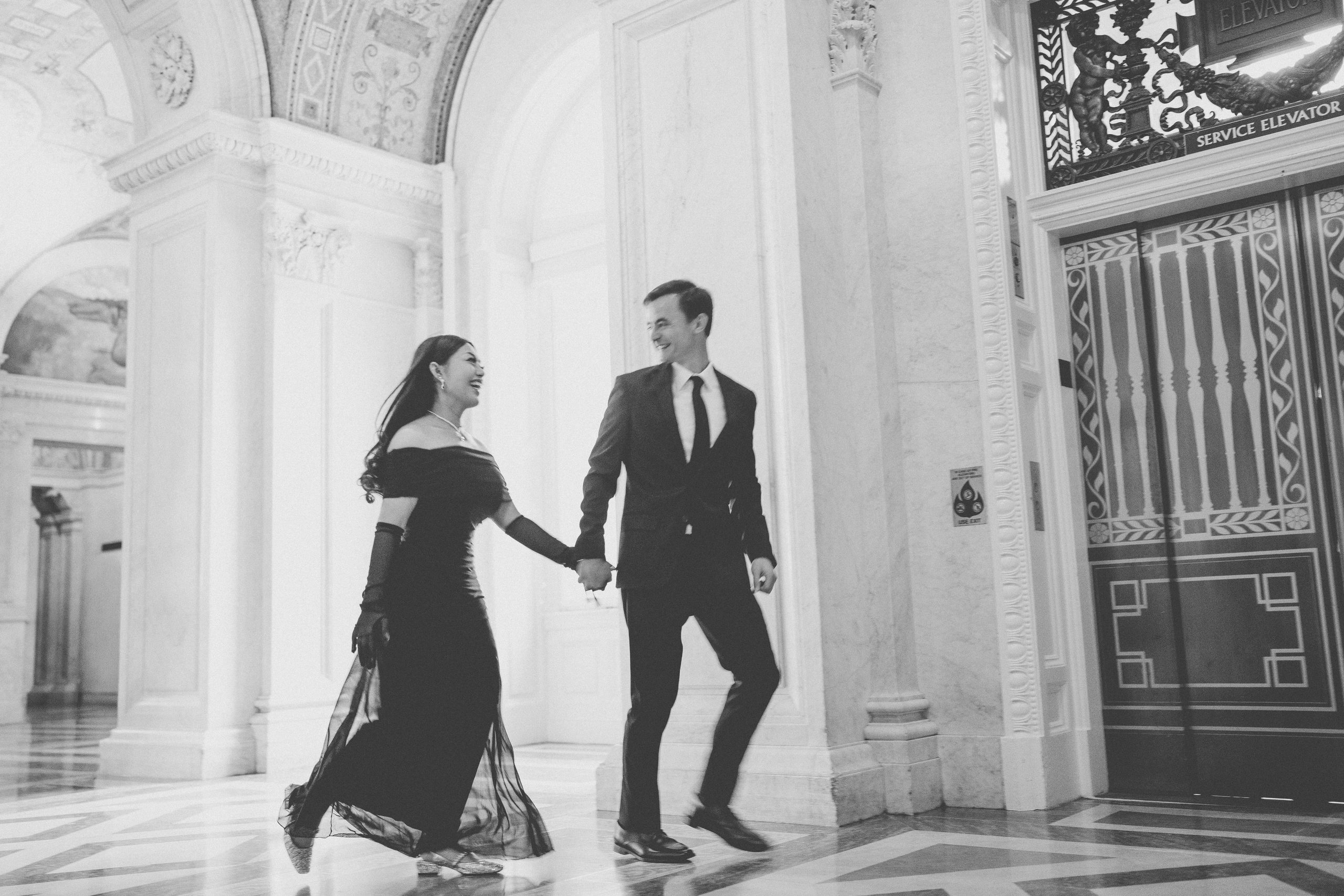 Black and white candid photo of a couple holding hands and laughing during their Library of Congress Engagement Photos.