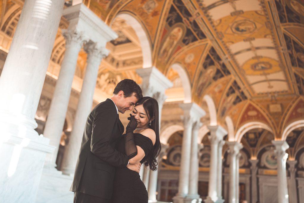 Couple embracing beneath the columns and detailed architecture during their Library of Congress Engagement Photos.