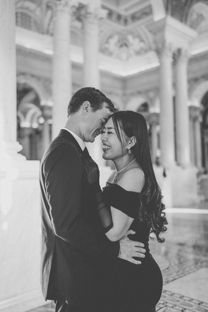 Black and white candid engagement photo of a couple laughing together inside the Library of Congress.