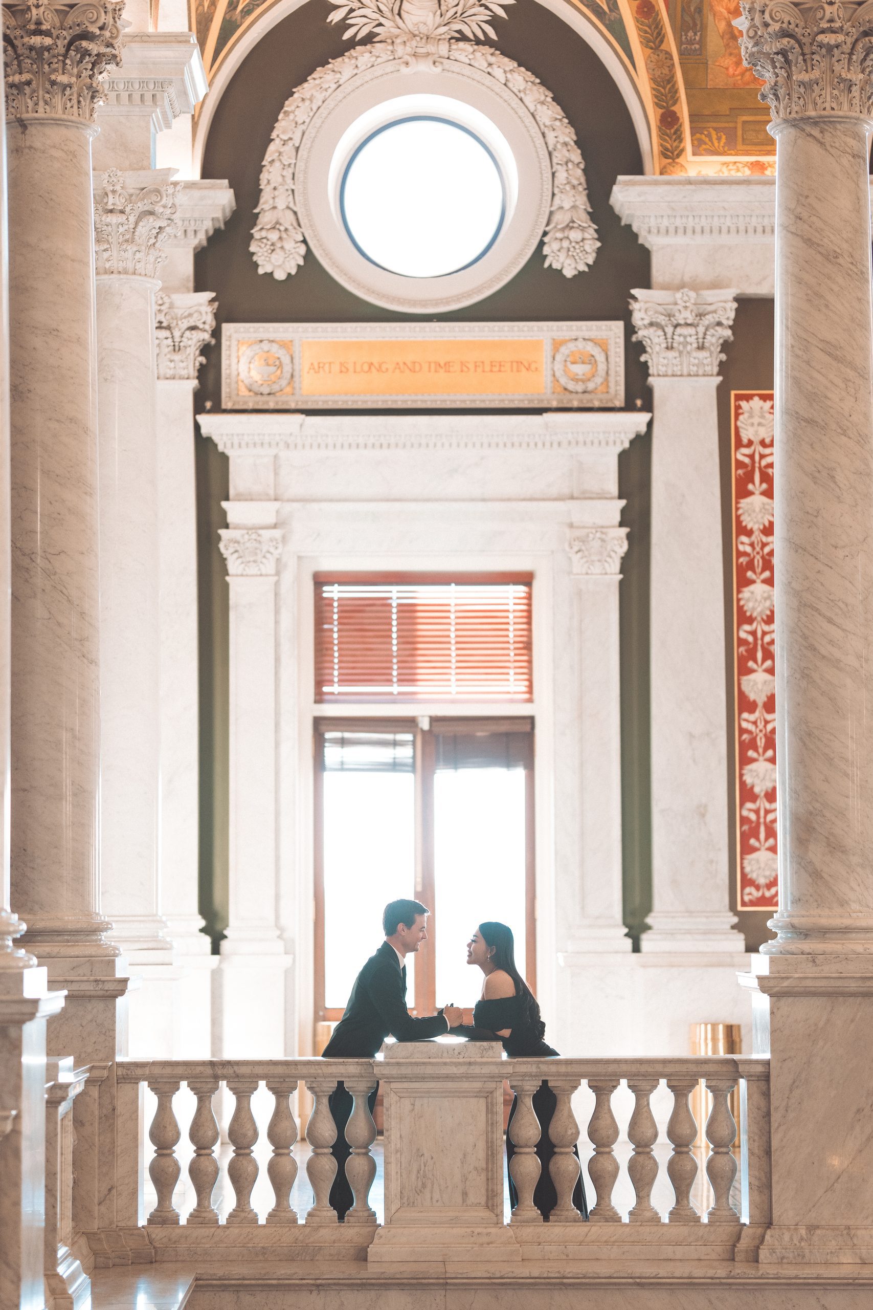 Couple leaning toward each other across a marble balcony inside the Library of Congress.