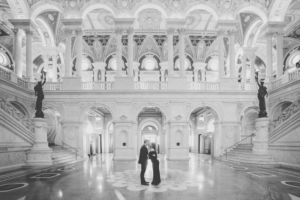 Black and white engagement photo of a couple kissing in the grand marble hall of the Library of Congress.