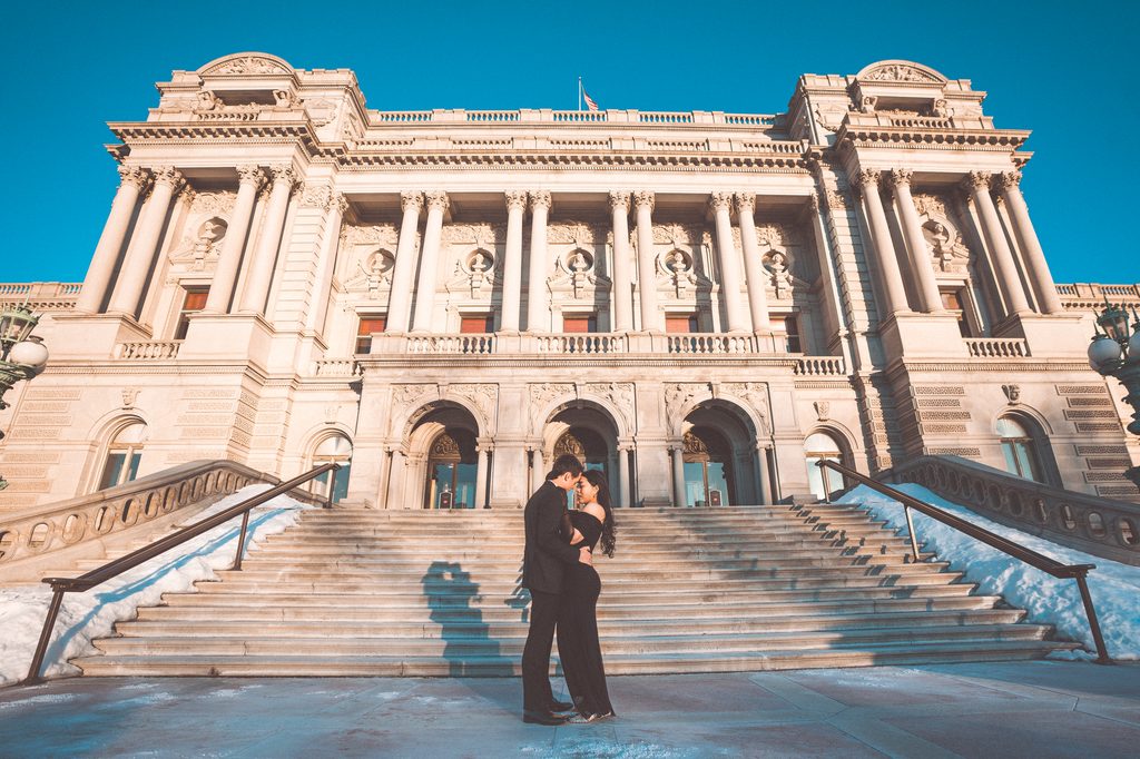 A couple dressed in black share an intimate moment while standing in front of the Library of Congress during the winter.