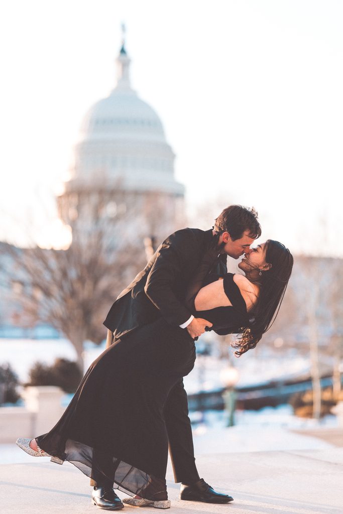 Couple sharing a playful dip and kiss outdoors with the U.S. Capitol in the background.