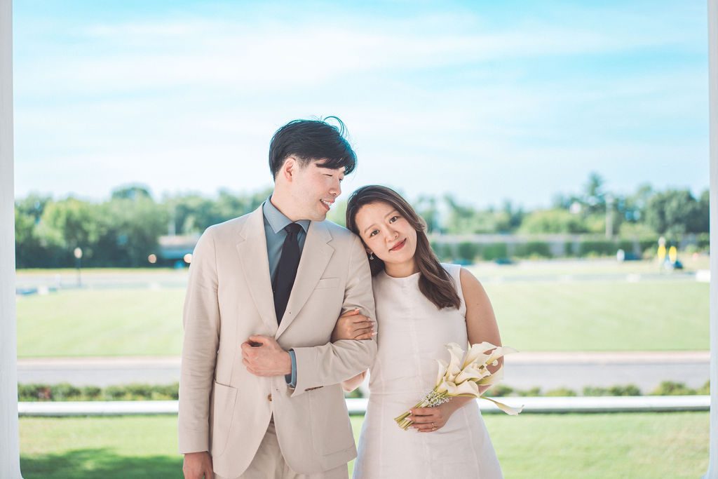 A couple smiling at the camera with blue skies and green grass behind them.