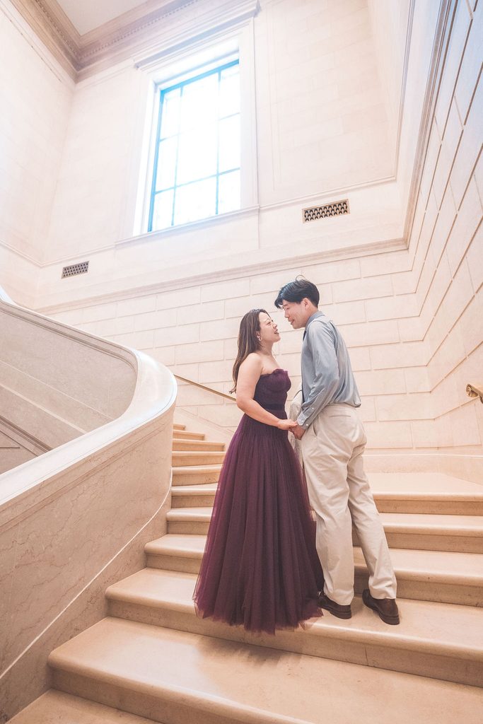National Gallery of Art engagement photos of a couple holding hands and smiling together on a sweeping marble staircase.
