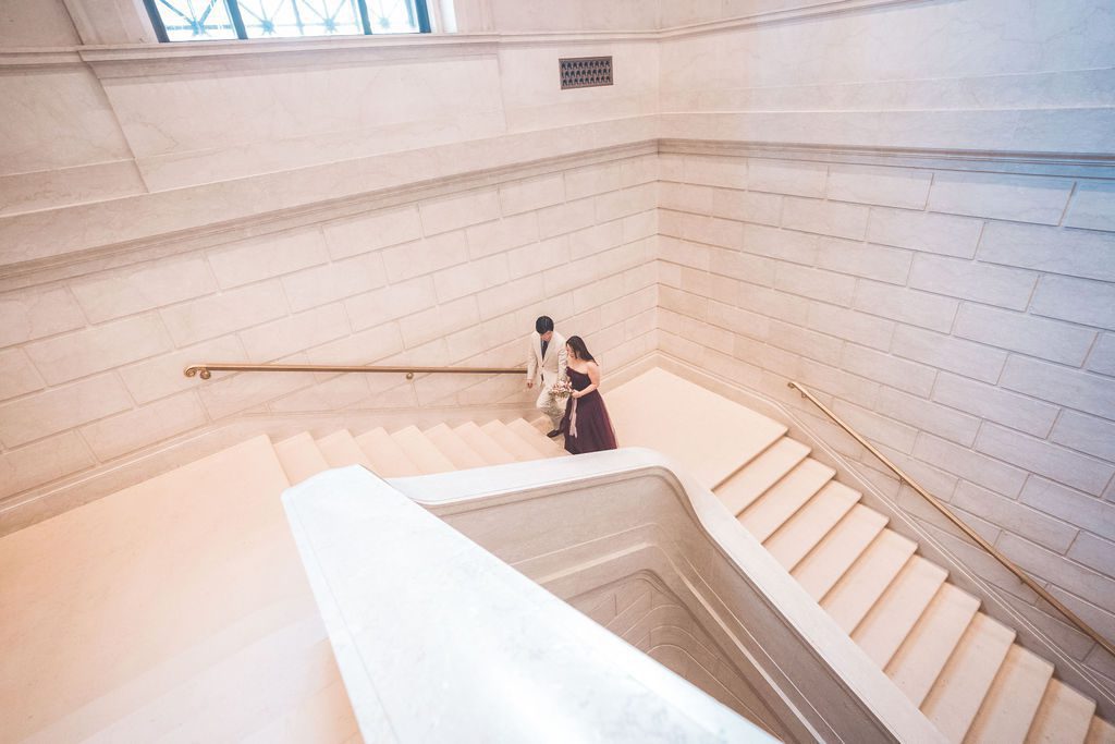 Couple walking together down a bright marble staircase inside the National Gallery of Art.
