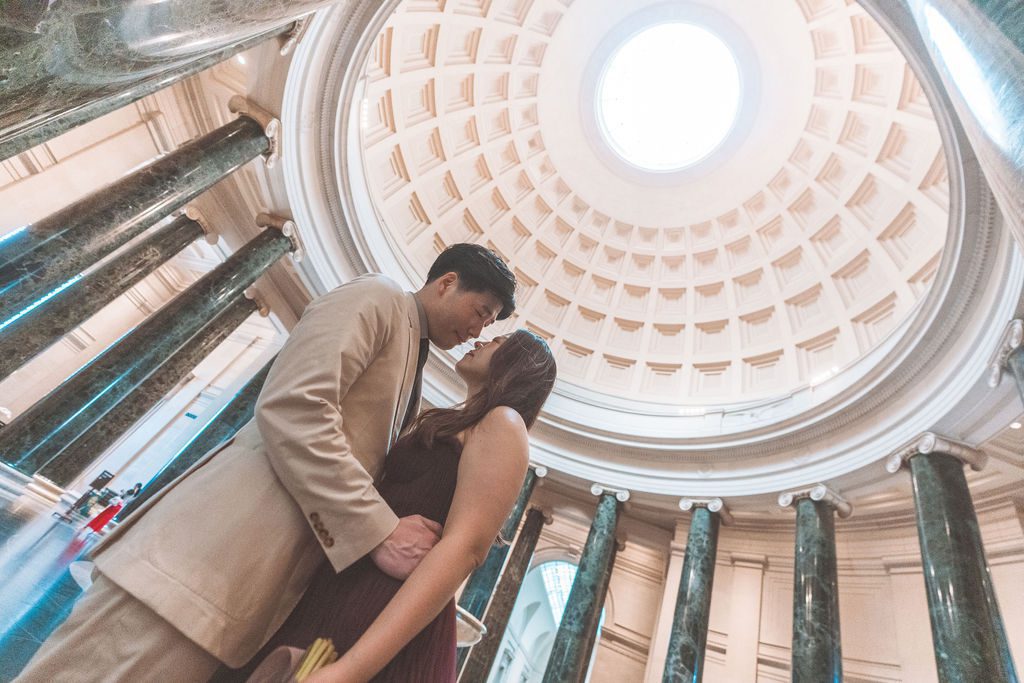 National Gallery of Art engagement photos of a couple sharing a quiet moment beneath the grand domed ceiling and marble columns.