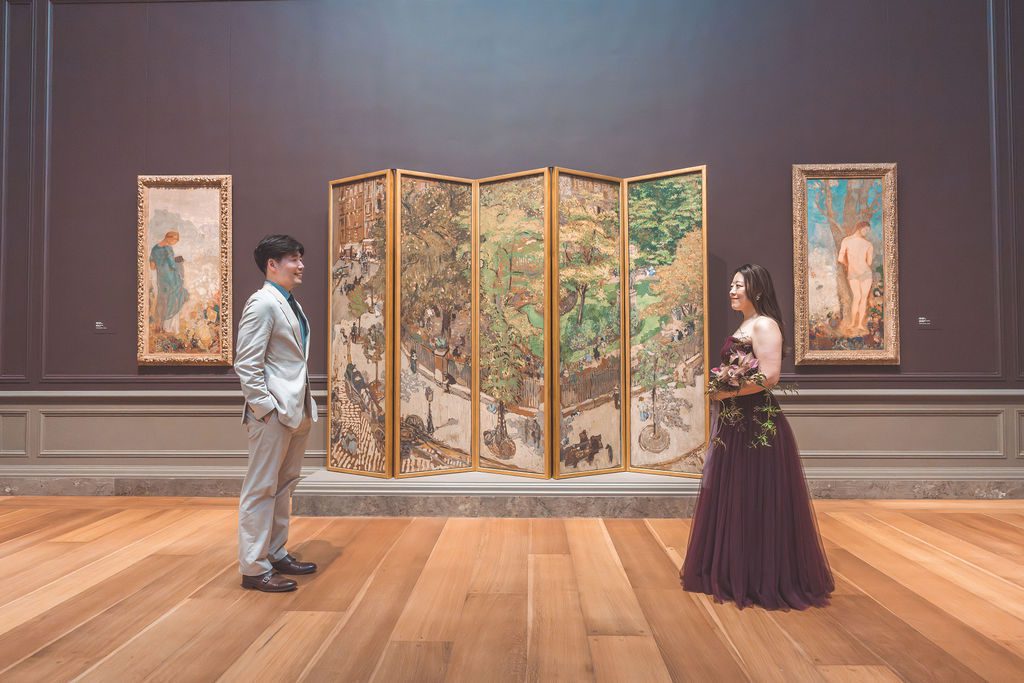 National Gallery of Art engagement photos of a couple facing each other across a gallery with a colorful decorative art screen behind them.