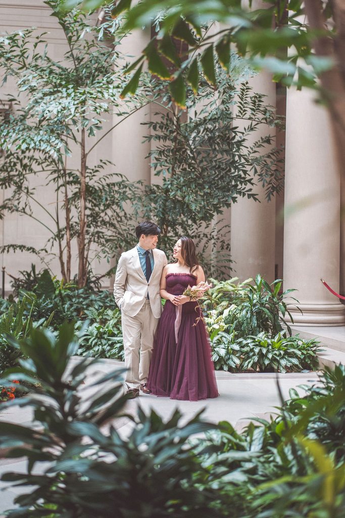 A couple look lovingly at each other with trees in the background.