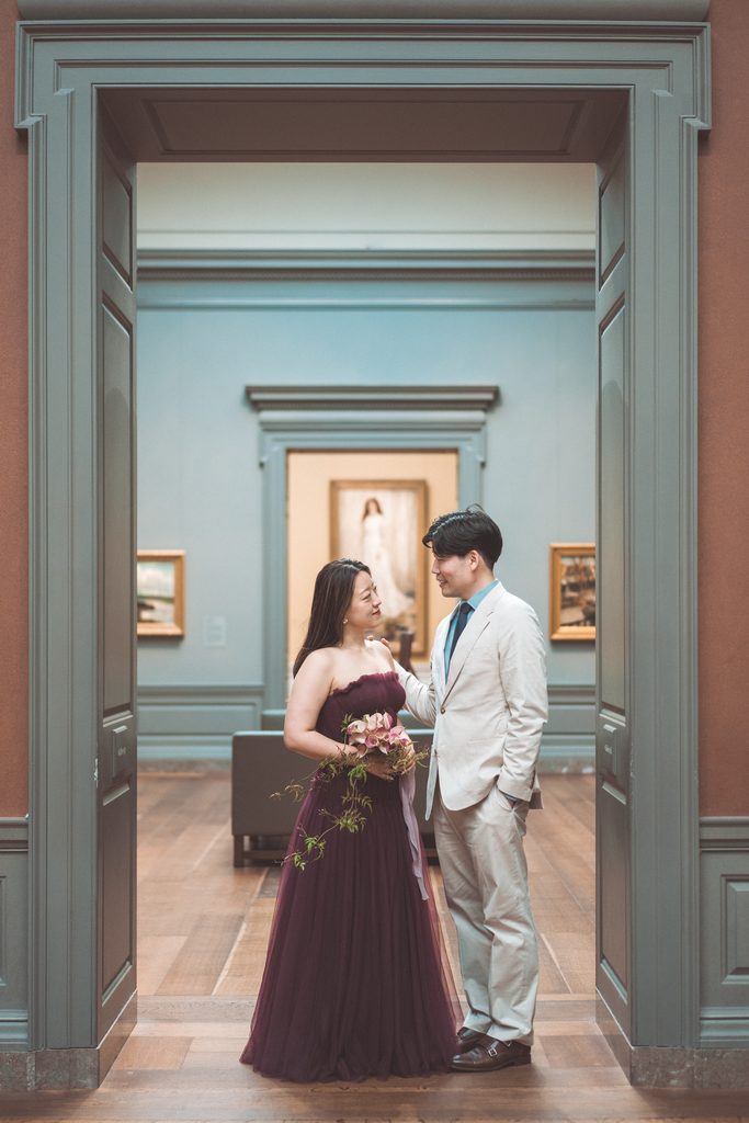 Couple standing together in a museum doorway framed by blue gallery walls and artwork.