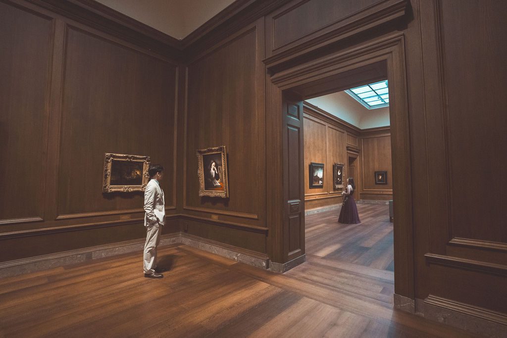 National Gallery of Art engagement photos of a couple standing in separate rooms framed by a doorway in a wood-paneled gallery.