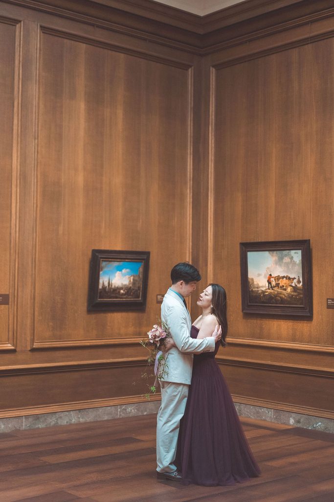 National Gallery of Art engagement photos of a couple embracing in a warm wood-paneled gallery surrounded by classic artwork.