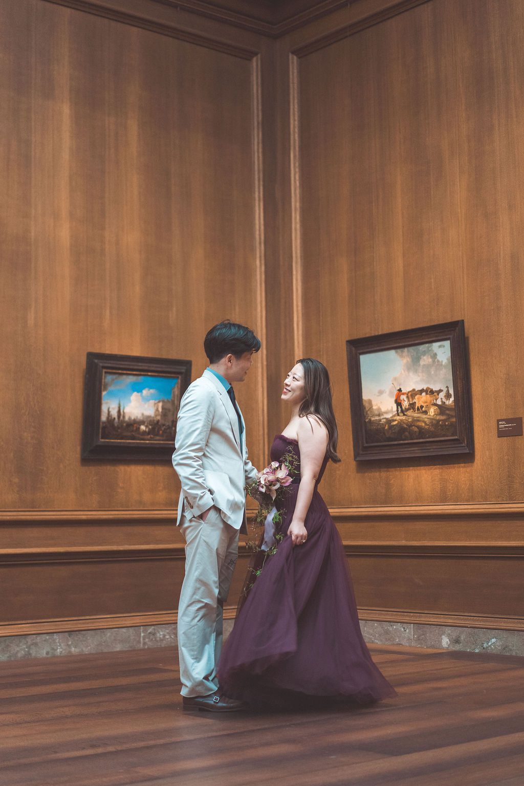 National Gallery of Art engagement photos of a couple laughing together in a wood-paneled gallery surrounded by classic artwork.