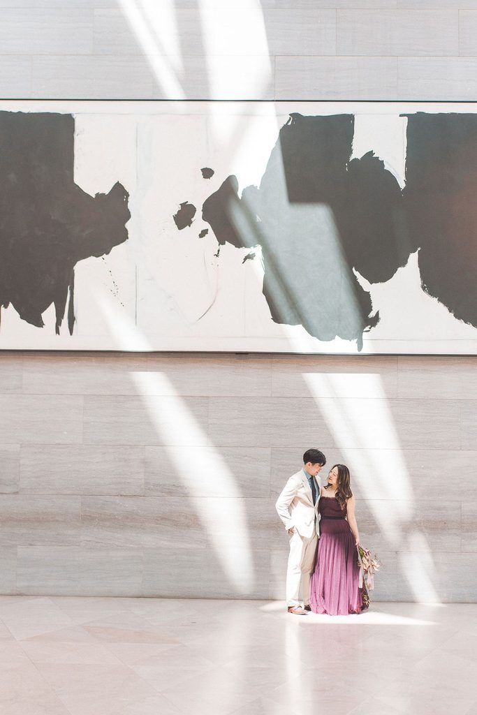 Couple standing beneath a large abstract painting with dramatic sunlight streaming across the museum wall.