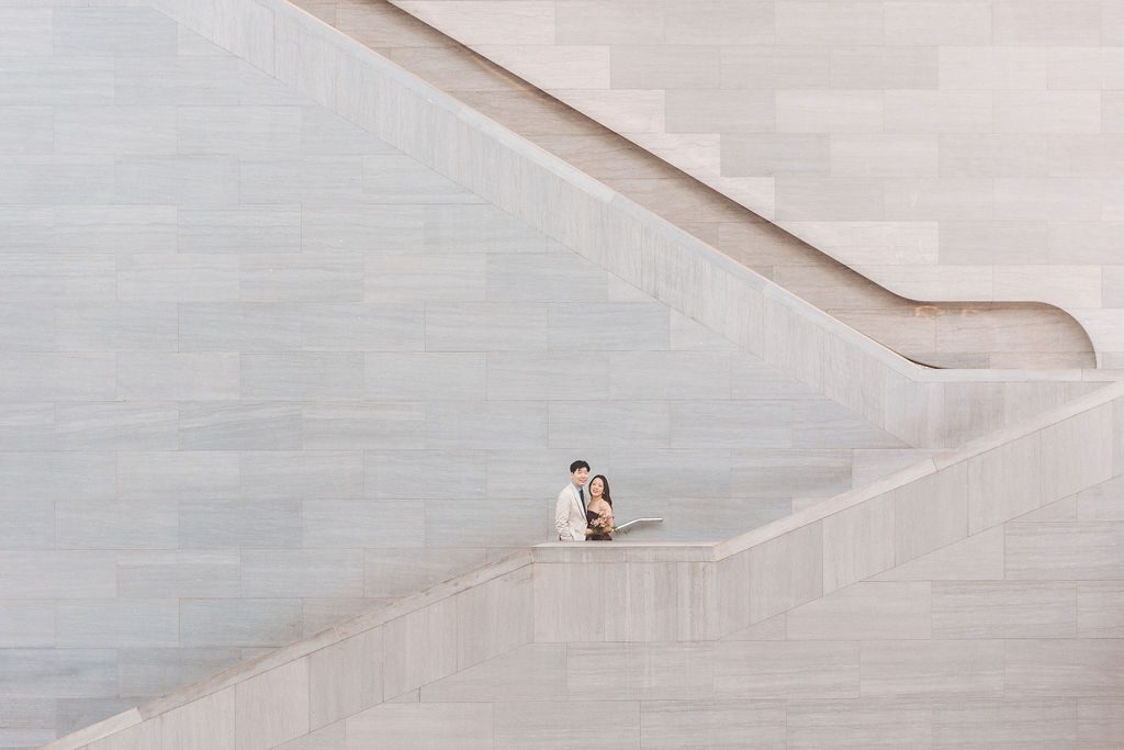 Couple framed within the geometric lines of a sweeping marble staircase inside the museum.