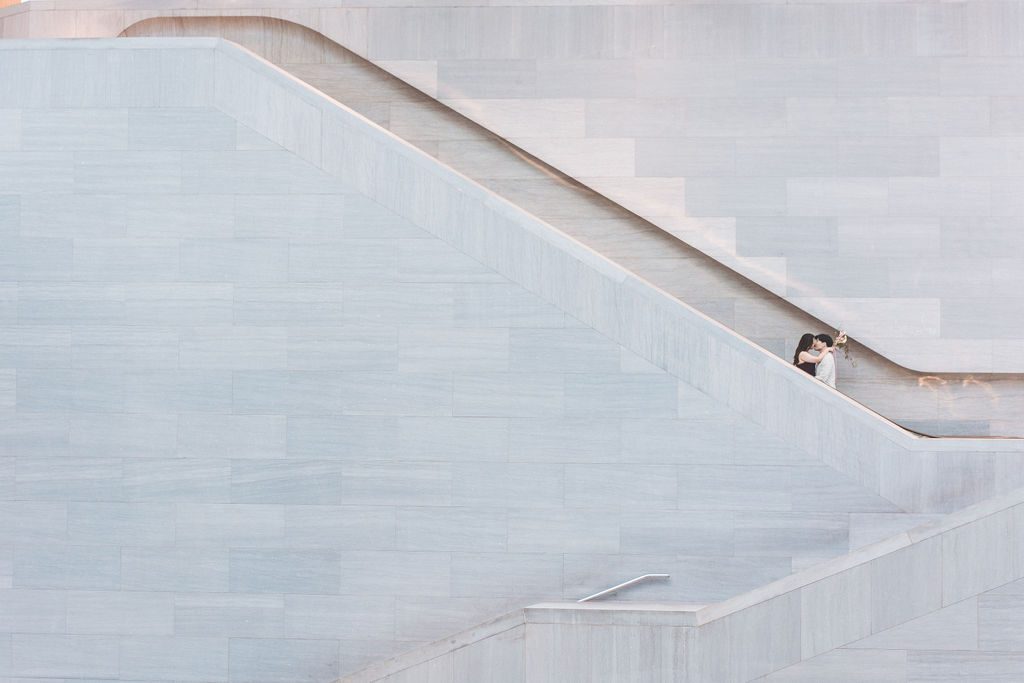 Couple framed within the geometric lines of a sweeping marble staircase inside the museum.