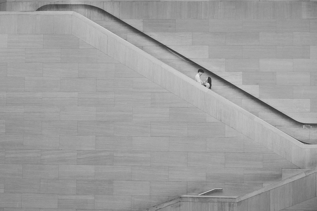 Black and white engagement portrait of a couple framed within the geometric lines of the National Gallery of Art staircase.